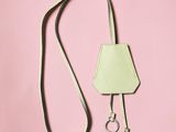 a white purse with a green strap on a pink background