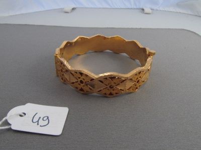 un bracelet en or posé sur un lit, avec une étiquette de prix accrochée dessus