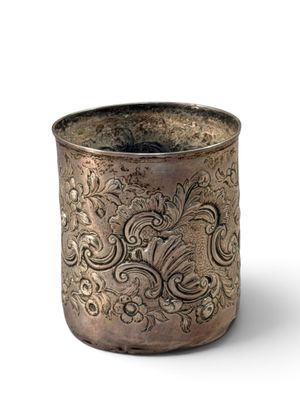 an old silver cup with a design on it on a white surface