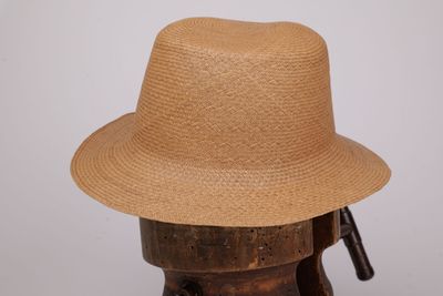 un chapeau de paille posé sur un support en bois, sur fond blanc