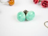 turquoise green glass stud earrings on a white surface surrounded by red flowers