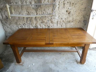 une table en bois sur laquelle reposent deux rallonges, devant un mur en pierre