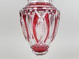 un vase en verre rouge posé sur un socle transparent, sur fond blanc
