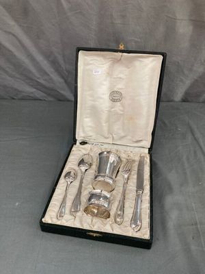 des couverts dans un coffret posé sur un lit, sur fond gris