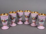 six pink vases with gold rims are lined up on a gray surface