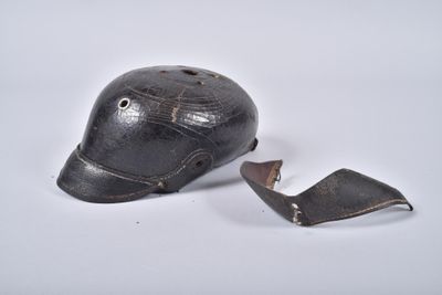 un vieux casque de baseball dont la visière est cassée, posé sur une surface blanche