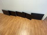 four black speakers sitting on top of a wooden floor next to a white wall