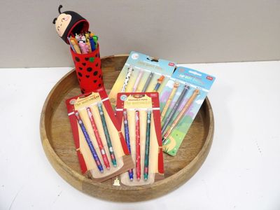 a wooden tray with pens, pencils, and a ladybug on it