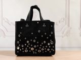 sac cabas noir clouté posé sur une table en bois devant un mur