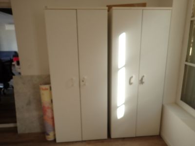 two white cupboards in the corner of a room with a window