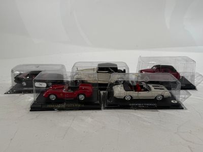 five toy cars in a display case on a white surface