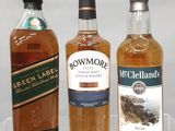 trois bouteilles de whisky posées sur une étagère en verre