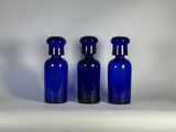 trois bouteilles en verre bleues sont alignées sur une surface blanche
