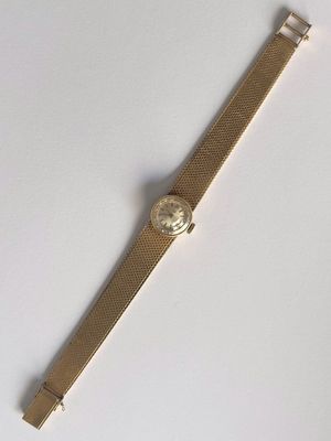 une image représentant une montre en or avec un cadran blanc posée sur une surface blanche