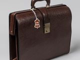 La mallette marron est posée sur une surface blanche sur laquelle est accrochée une étiquette.