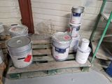 Plusieurs seaux de peinture sont posés sur une palette dans une pièce.