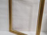 a gold picture frame sitting on a white surface next to a vase