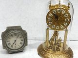 two clocks sitting next to each other under a glass dome