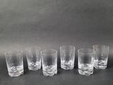 six clear glass tumblers lined up in a row on a black surface