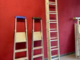 Plusieurs échelles sont appuyées contre un mur rouge dans une pièce.
