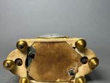 an antique brass clock with a glass face on a gray surface