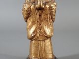 statue en or représentant une femme, les mains jointes, assise sur un rocher