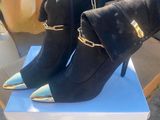 une paire de bottes à talons hauts noires et dorées posées sur une boîte blanche