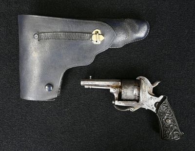un pistolet posé à côté d'un étui, sur fond noir