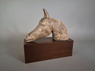 sculpture of a horse head on a wooden base against a gray background
