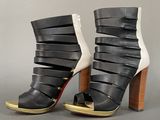 black and white high heeled sandals with gold accents on a grey background