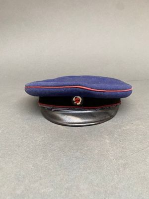 une casquette bleue à bordure rouge posée sur un socle en métal, sur une table