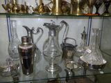 a glass shelf with a lot of silver vases on it