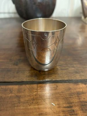 une coupe en argent posée sur une table en bois, avec un vase en arrière-plan