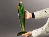 someone is holding a green glass vase in their hand on a gray background