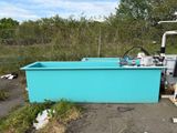 une cuve bleue contenant une machine, posée dans la terre