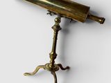 un télescope ancien en laiton posé sur un trépied, sur fond blanc