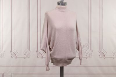 un pull à col roulé rose sur un mannequin posé devant un mur blanc