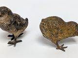 two small metal birds are standing next to each other on a white surface