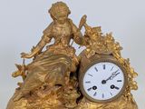 a gold clock with a woman sitting on it