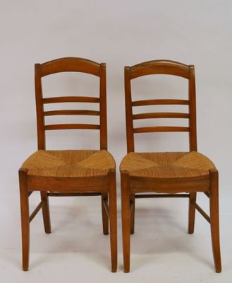 pair of wooden chairs with wicker seats against a white backdrop