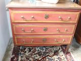 a pink dresser with gold hardware and a white vase on top of it