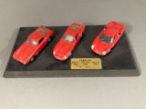 Trois petites voitures rouges sont exposées sur un socle noir