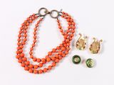 an orange beaded necklace with a pair of earrings on a white surface