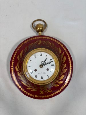 a red and gold clock hanging on a white wall