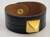 bracelet à manchette en cuir orné de clous pyramidaux dorés sur un fond blanc