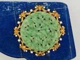 broche en jade vert et diamants posée sur un plateau bleu