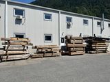 Plusieurs piles de bois sont empilées devant un bâtiment, avec une montagne en arrière-plan.