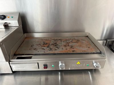 un plan de travail en acier inoxydable sur lequel est posée une plaque à pizza, avec une cuisinière à l'arrière-plan