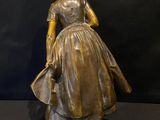 bronze statue of a woman in a dress and hat on a rock