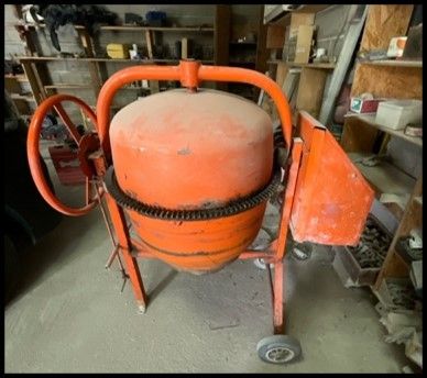 une bétonnière orange garée dans un garage, à côté d'une étagère remplie d'outils